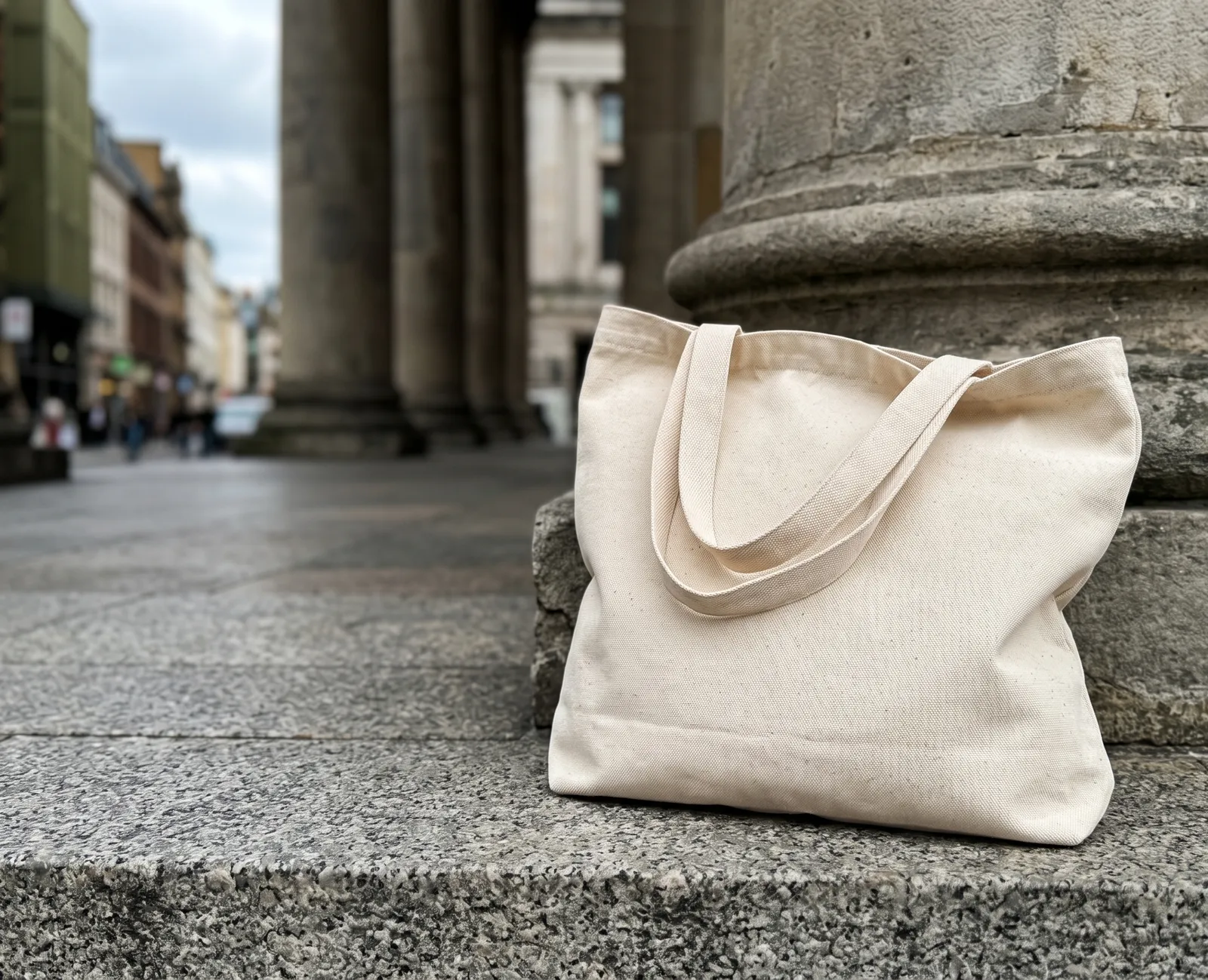 Blank canvas tote resting on a granite step beside a stone column
